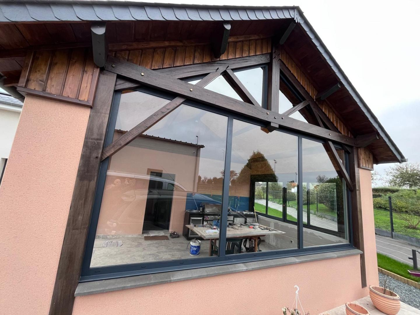 Grande baie fixe gris anthracite sous pignon vitré en bois, façade saumon