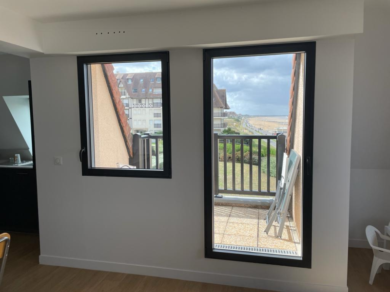 Fenêtres à cadres anthracite dans un intérieur blanc, vue sur balcon et littoral