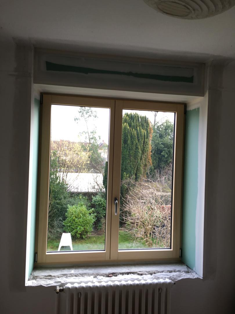 Fenêtre bois clair à deux vantaux en cours de pose, radiateur blanc et jardin
