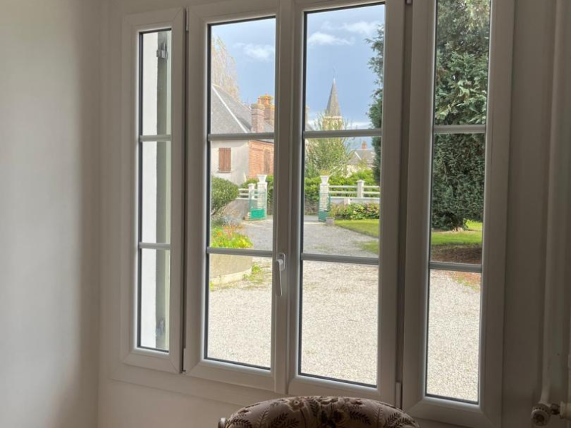 Fenêtre PVC blanche à quatre vantaux et petits bois avec vue sur clocher