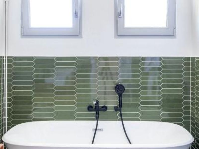 Deux fenêtres carrées à cadres gris au-dessus d'une baignoire blanche, carrelage vert