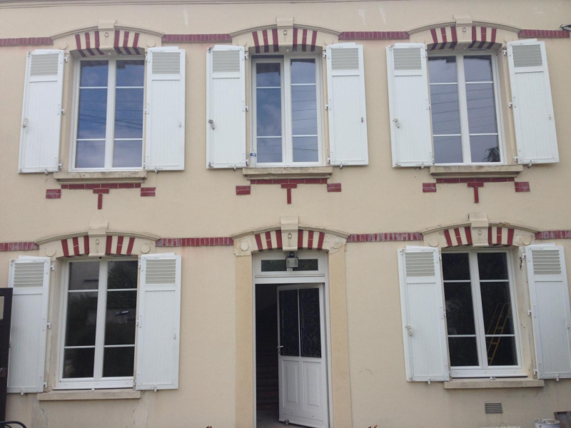 Fenêtres PVC blanches à petits bois et volets ouverts sur façade crème