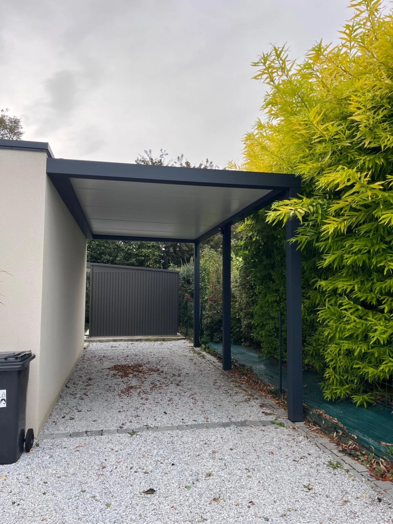 Carport blanc adossé à une maison saumon, camping-car argenté dessous