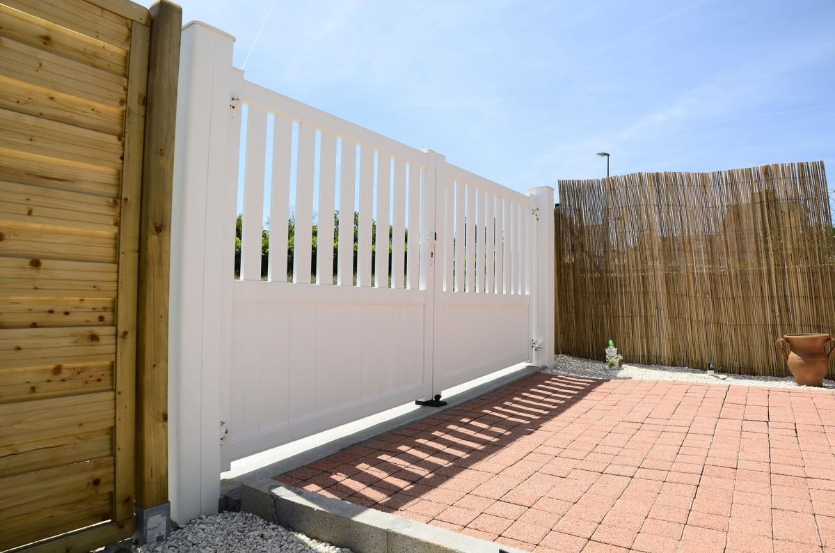 Portail battant blanc plein en bas et à barreaux en haut entre poteaux blancs