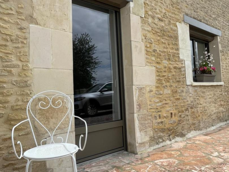 Porte-fenêtre à cadre brun foncé dans une façade en pierres, terrasse dallée et jardinière