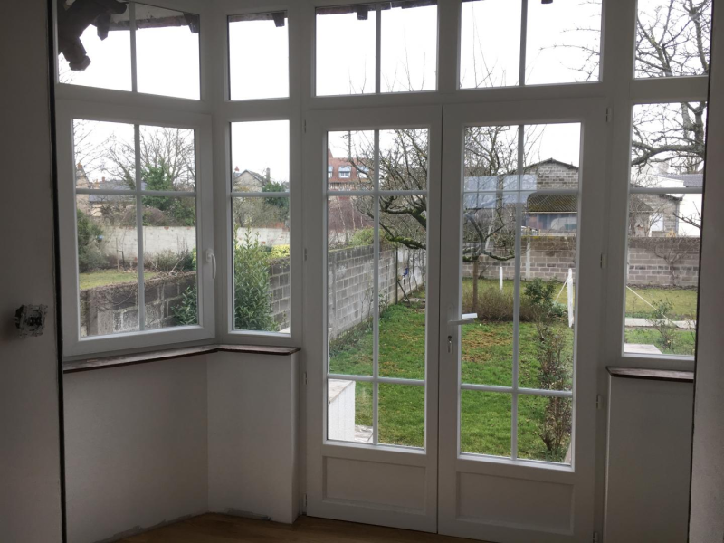 Porte-fenêtre PVC blanche à petits bois ouvrant sur un jardin