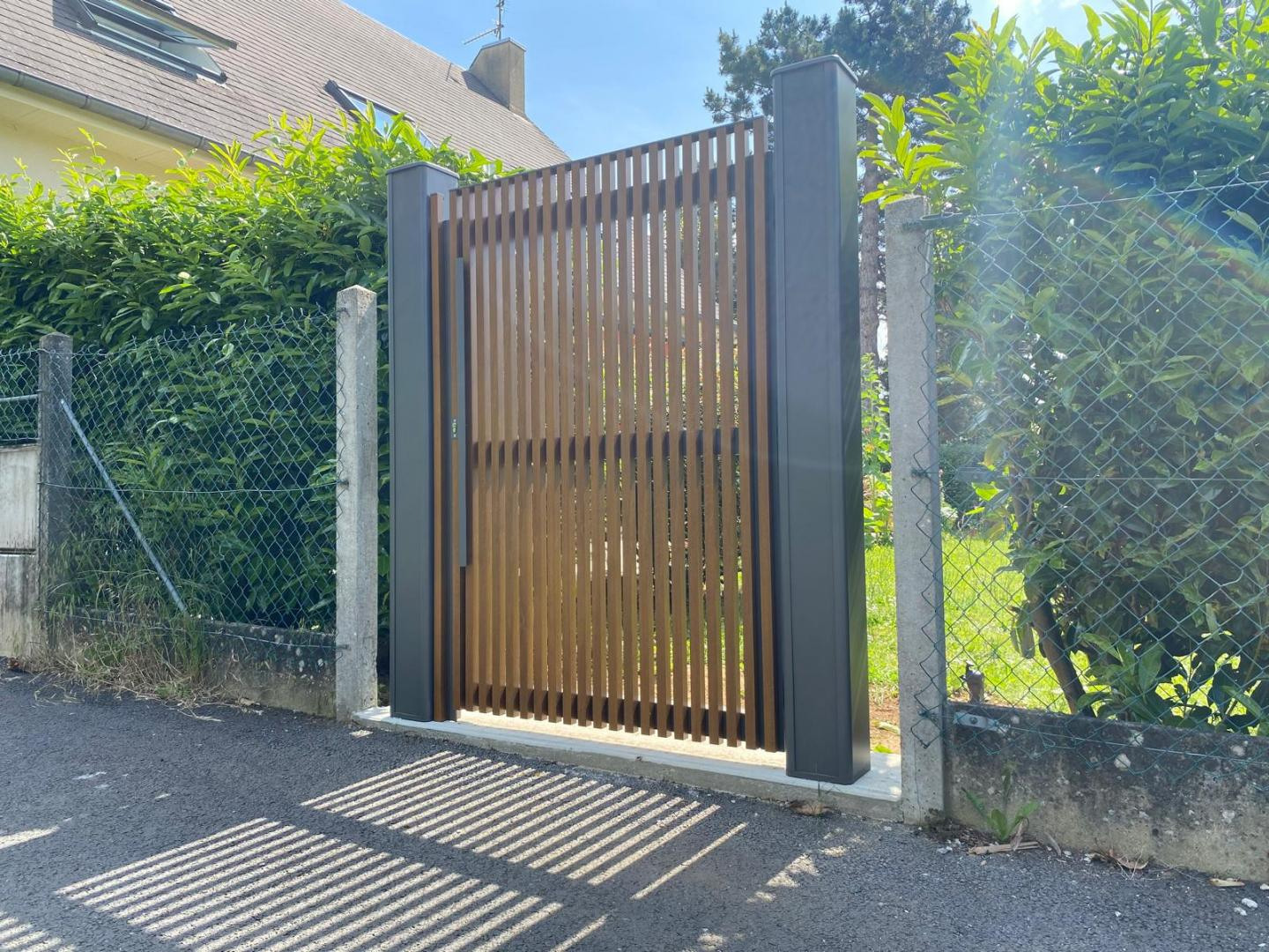 Portillon à lames bois verticales et cadre anthracite entre poteaux gris