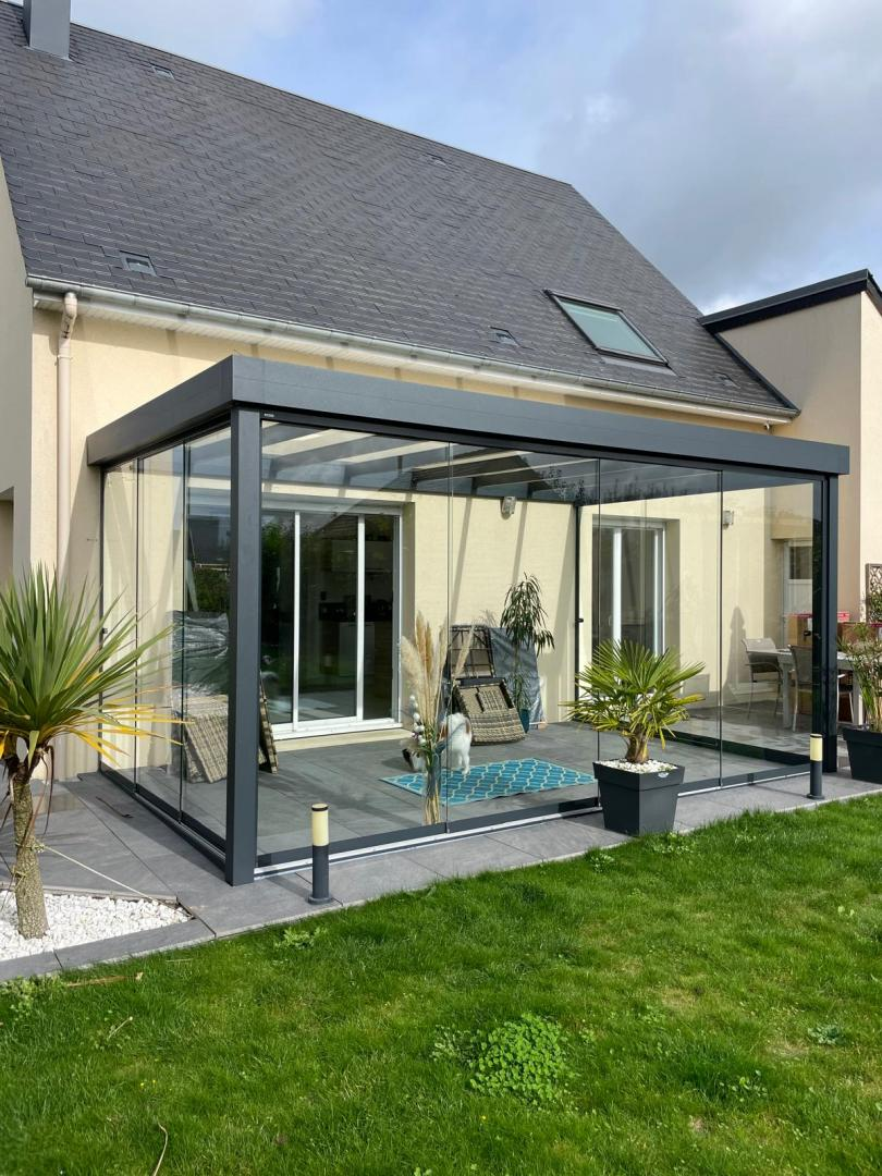Véranda aluminium anthracite vitrée sur terrasse carrelée devant maison crème