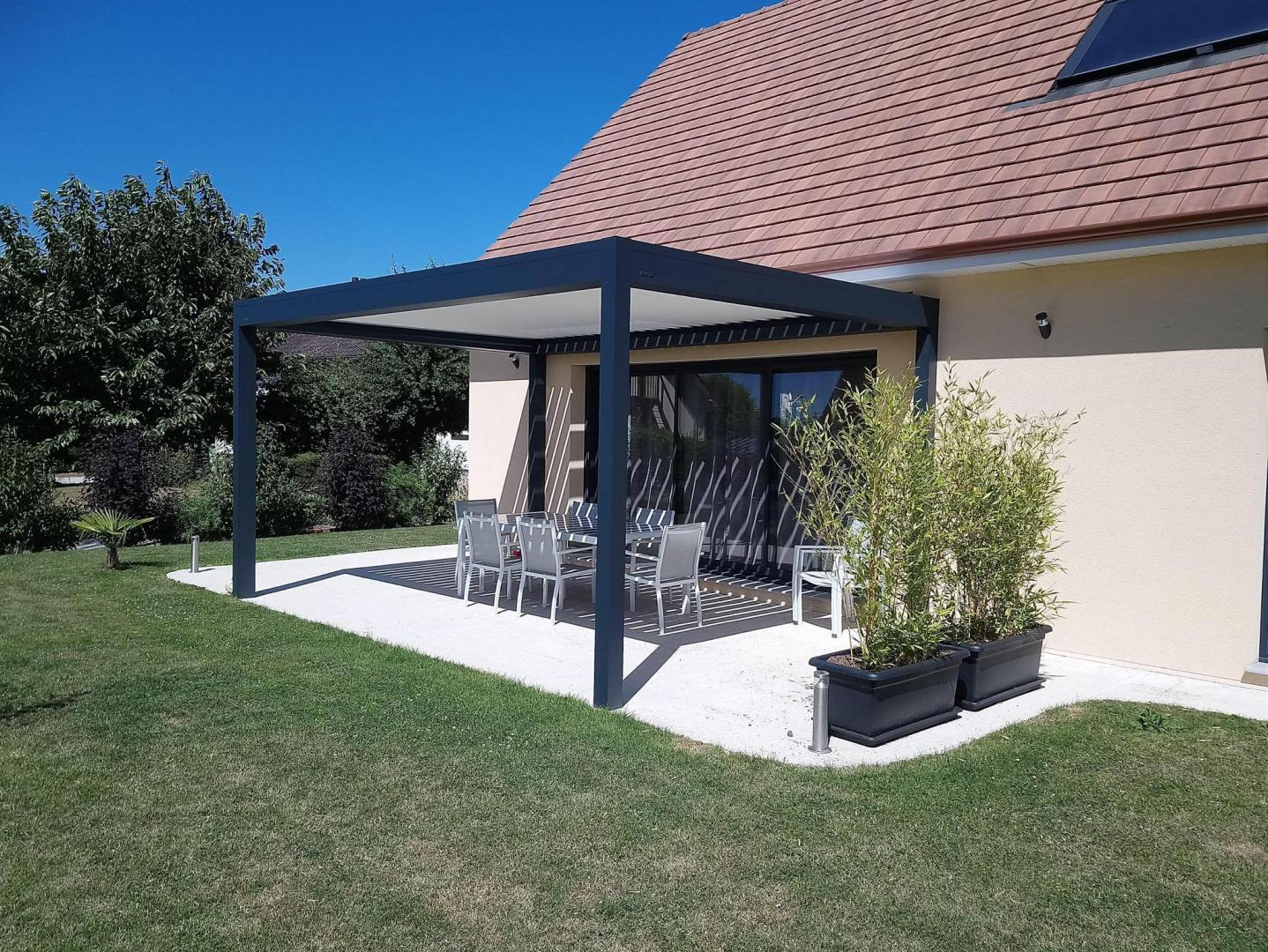 Pergola bioclimatique aluminium anthracite adossée à une maison, terrasse claire