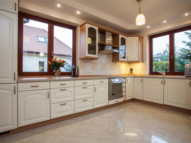 Fenêtres aspect bois brun foncé dans une cuisine crème, vue maison et verdure
