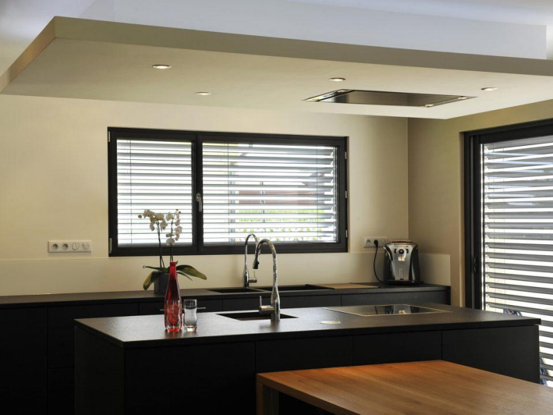 Brise-soleil orientables gris devant fenêtres noires dans une cuisine moderne