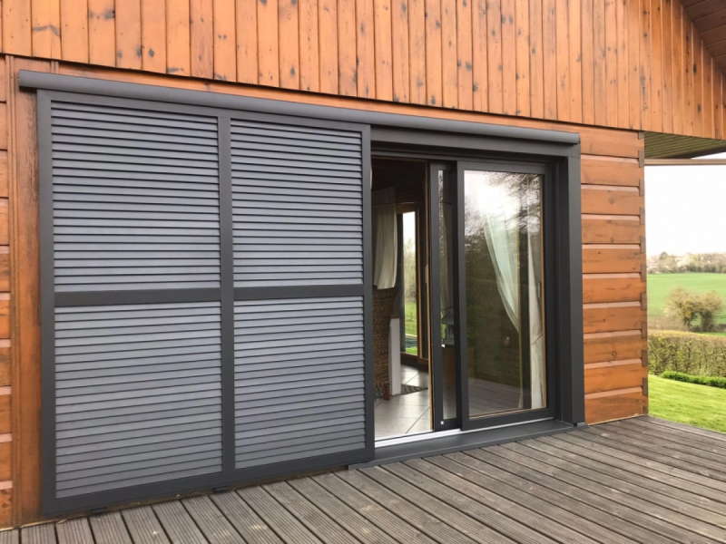 Volets coulissants anthracite à lames horizontales devant baie sur terrasse bois
