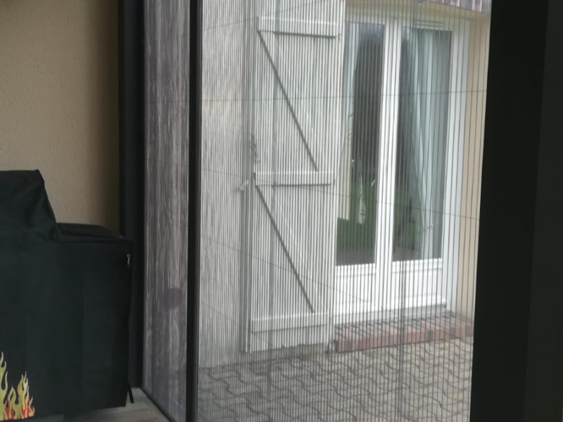 Moustiquaire plissée grise dans cadre anthracite, vue sur cour pavée