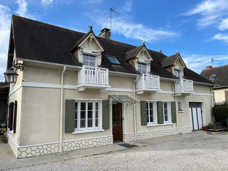 Maison beige avec volets verts, lucarnes blanches et porte d'entrée en bois