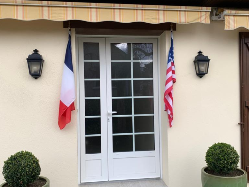 Porte d'entrée blanche à petits bois et vitrages, appliques noires et pots verts