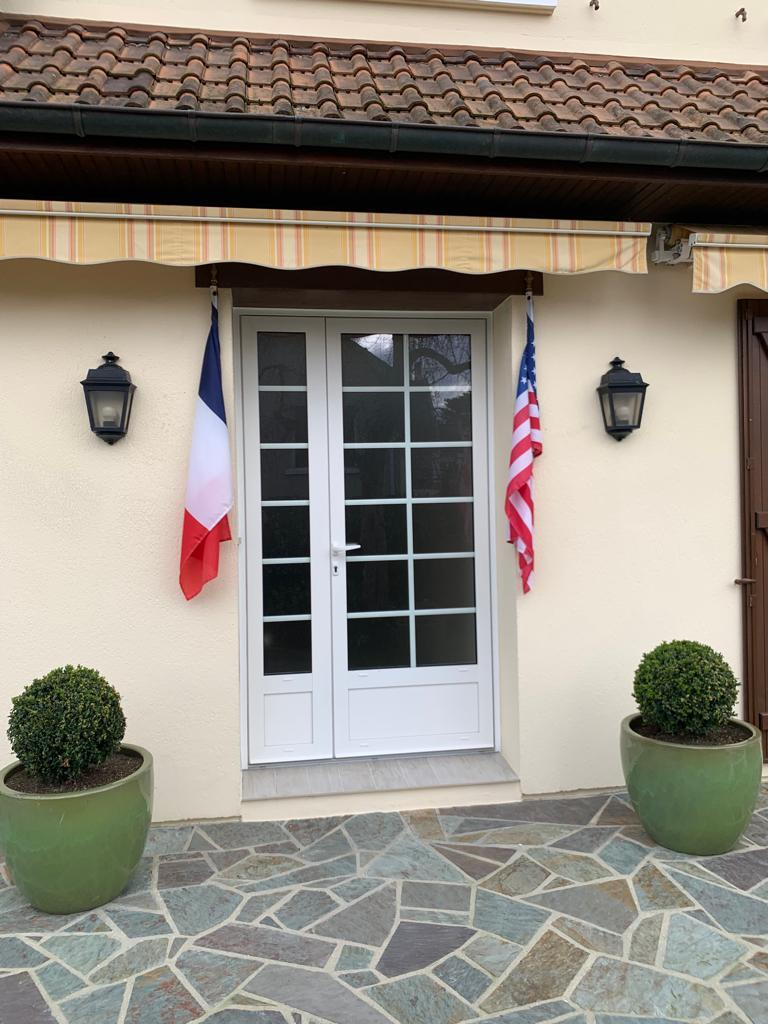Porte d'entrée blanche à petits bois et vitrages, appliques noires et pots verts