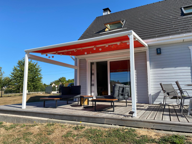 Pergola blanche à toile rouge déployée sur terrasse bois, mobilier de jardin