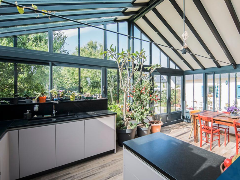 Véranda aluminium anthracite avec cuisine et table bois, vue sur jardin