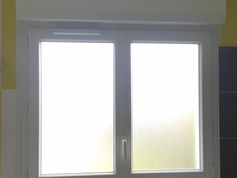 Fenêtre PVC blanche à vitrage dépoli et coffre de volet roulant, mur jaune